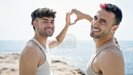 Téléchargez les photos : Deux hommes couple se serrant dans leurs bras en faisant un geste cardiaque au bord de la mer - en image libre de droit