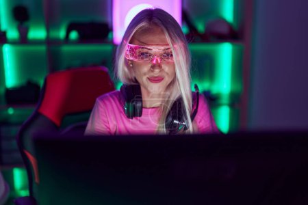Young blonde woman streamer using computer and virtual reality glasses at gaming room