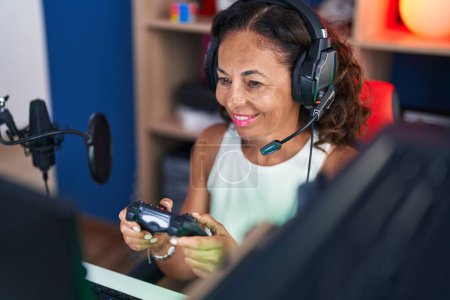 Téléchargez les photos : Femme du moyen âge streamer jouer à un jeu vidéo en utilisant joystick à la salle de jeu - en image libre de droit