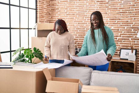 Téléchargez les photos : African american women smiling confident looking house plans at new home - en image libre de droit