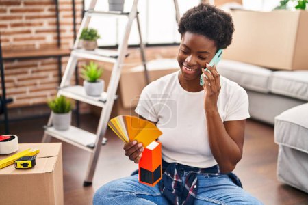 Téléchargez les photos : Femme afro-américaine parlant sur le smartphone choisir la couleur de peinture à la nouvelle maison - en image libre de droit