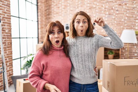 Photo for Mother and daughter moving to a new home holding keys scared and amazed with open mouth for surprise, disbelief face - Royalty Free Image