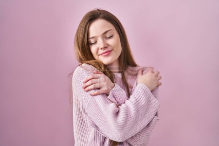 Photo for Young caucasian woman standing over pink background hugging oneself happy and positive, smiling confident. self love and self care - Royalty Free Image