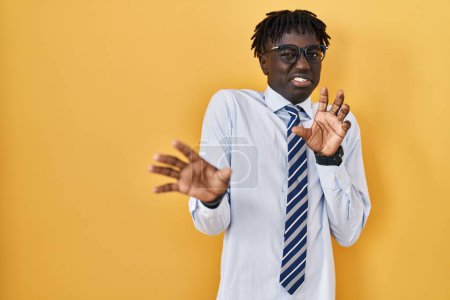 Foto de Hombre africano con rastas de pie sobre fondo amarillo expresión disgustada, disgustado y temeroso haciendo cara de asco porque la reacción de aversión. con las manos levantadas - Imagen libre de derechos