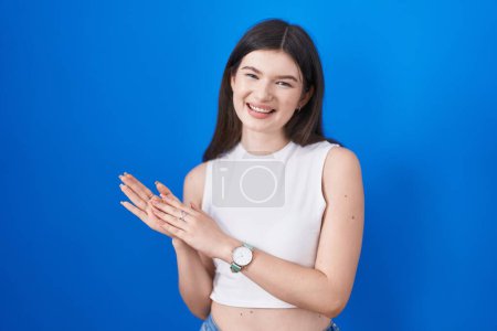 Téléchargez les photos : Jeune femme caucasienne debout sur fond bleu applaudissant heureux et joyeux, souriant mains fières ensemble - en image libre de droit
