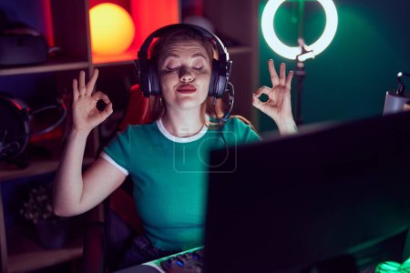 Photo for Redhead woman playing video games relax and smiling with eyes closed doing meditation gesture with fingers. yoga concept. - Royalty Free Image
