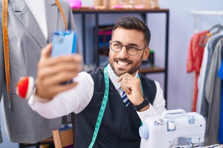 Téléchargez les photos : Young hispanic man tailor smiling confident make selfie by smartphone at tailor shop - en image libre de droit