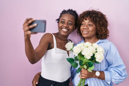 Téléchargez les photos : Deux femmes africaines prenant une photo selfie avec des fleurs souriant avec un sourire heureux et cool sur le visage. montrant les dents. - en image libre de droit