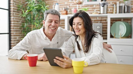 Téléchargez les photos : Senior homme et femme couple souriant confiant regarder la vidéo sur touchpad à la salle à manger - en image libre de droit