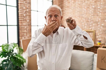 Téléchargez les photos : Homme âgé avec les cheveux gris tenant monnaie virtuelle Bitcoin couvrant la bouche avec la main, choqué et peur de l'erreur. expression surprise - en image libre de droit