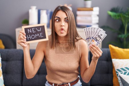 Photo for Young hispanic woman holding blackboard with new home text and dollars making fish face with mouth and squinting eyes, crazy and comical. - Royalty Free Image