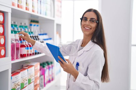 Photo for Young beautiful hispanic woman pharmacist using touchpad working at pharmacy - Royalty Free Image
