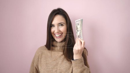Photo for Beautiful hispanic woman smiling confident holding dollars over isolated pink background - Royalty Free Image