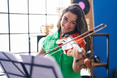 Photo for Young hispanic woman musician smiling confident playing violin at music studio - Royalty Free Image