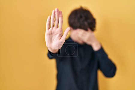 Photo for Young man wearing glasses over yellow background covering eyes with hands and doing stop gesture with sad and fear expression. embarrassed and negative concept. - Royalty Free Image