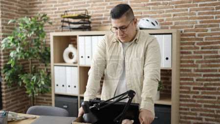 Photo for Young hispanic man being fired packing belongings from workplace at office - Royalty Free Image