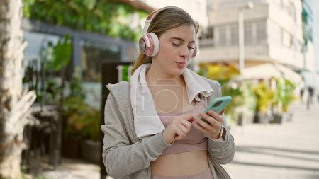 Photo for Young blonde woman wearing sportswear listening to music at street - Royalty Free Image