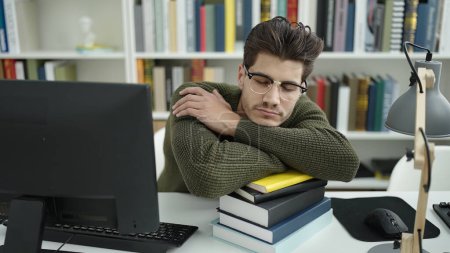 Téléchargez les photos : Jeune homme hispanique étudiant dormant avec la tête sur les livres à l'université de la bibliothèque - en image libre de droit