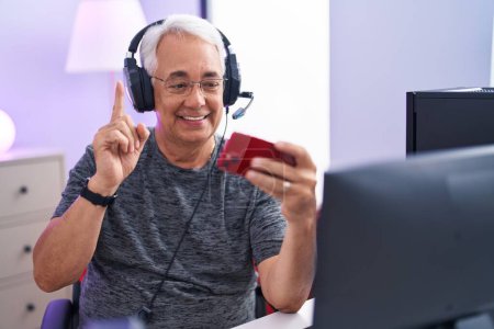 Photo for Middle age man with grey hair playing video games with smartphone smiling with an idea or question pointing finger with happy face, number one - Royalty Free Image