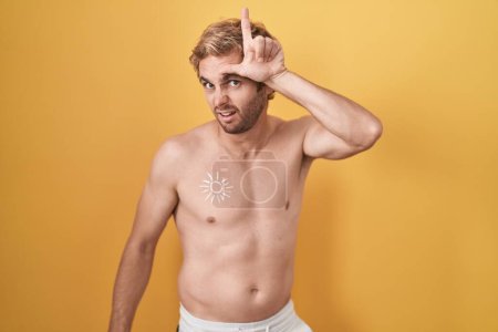 Téléchargez les photos : Homme caucasien debout torse nu portant un écran solaire se moquant des gens avec les doigts sur le front faisant geste perdant moquerie et insultant. - en image libre de droit