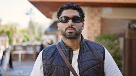 Téléchargez les photos : Homme afro-américain debout avec une expression sérieuse portant des lunettes de soleil à la terrasse du café - en image libre de droit