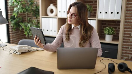 Photo for Young beautiful hispanic woman business worker using touchpad and laptop at office - Royalty Free Image