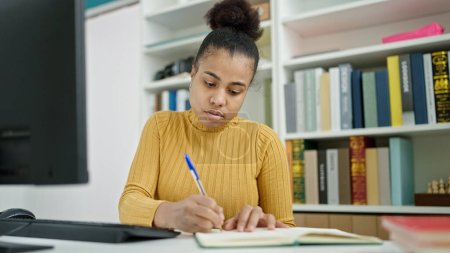 Photo for Young african american woman student using computer taking notes at the library - Royalty Free Image