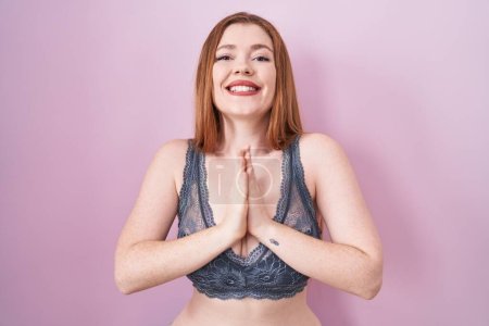Photo for Redhead woman wearing lingerie over pink background praying with hands together asking for forgiveness smiling confident. - Royalty Free Image