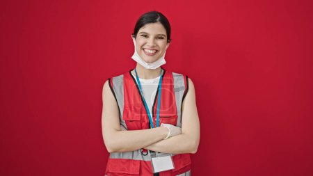 Téléchargez les photos : Jeune belle femme hispanique médecin portant un masque médical debout avec les bras croisés geste sur fond rouge isolé - en image libre de droit