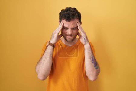Foto de Hombre hispano joven de pie sobre fondo amarillo con la mano en la cabeza, dolor de cabeza porque el estrés. padecer migraña. - Imagen libre de derechos