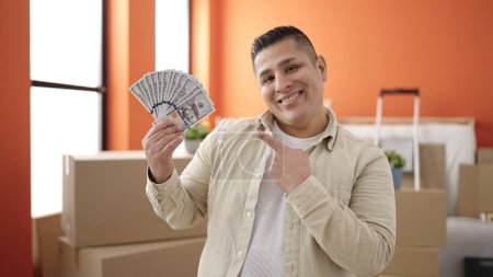 Foto de Joven hombre hispano sonriendo confiado señalando dinero en nuevo hogar - Imagen libre de derechos