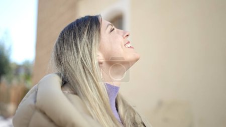 Téléchargez les photos : Jeune femme blonde souriante confiante regardant le ciel dans la rue - en image libre de droit