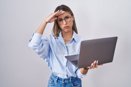 Photo for Young woman working using computer laptop worried and stressed about a problem with hand on forehead, nervous and anxious for crisis - Royalty Free Image
