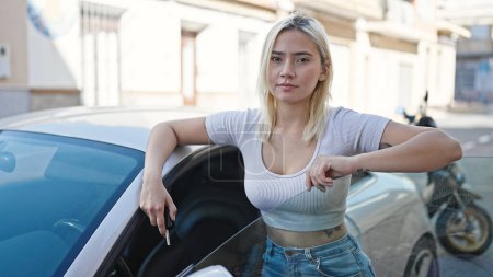 Foto de Joven hermosa mujer hispana apoyada en la puerta del coche sosteniendo llaves en la calle - Imagen libre de derechos