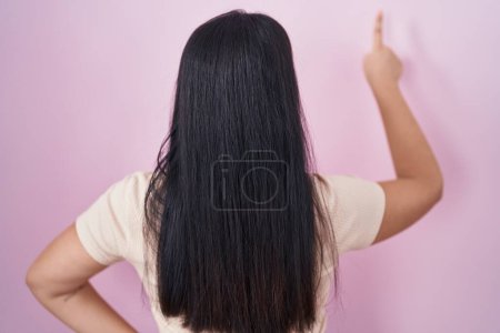 Photo for Young hispanic woman standing over pink background posing backwards pointing ahead with finger hand - Royalty Free Image