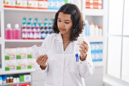 Foto de Joven mujer farmacéutica sosteniendo pastillas botella lectura prescripción en la farmacia - Imagen libre de derechos