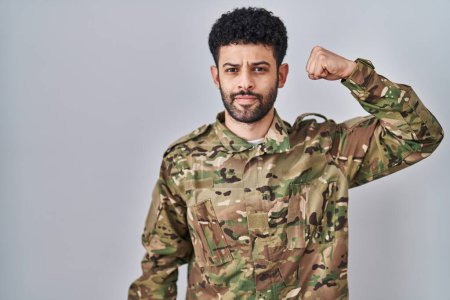 Téléchargez les photos : Arabe homme portant camouflage uniforme de l'armée personne forte montrant muscle du bras, confiant et fier de la puissance - en image libre de droit