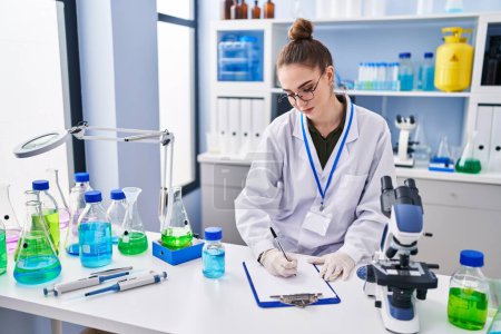 Téléchargez les photos : Jeune femme scientifique mesurant l'écriture liquide sur document au laboratoire - en image libre de droit