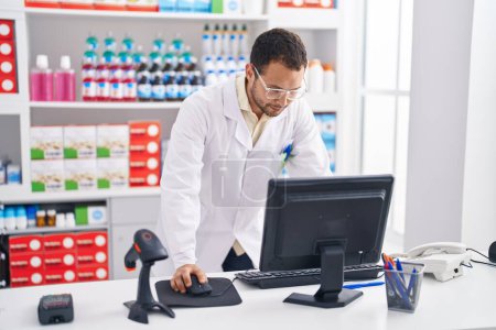 Photo for Young man pharmacist using computer working at pharmacy - Royalty Free Image