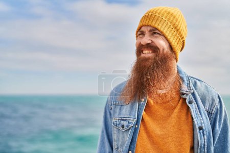 Téléchargez les photos : Jeune rousse homme souriant confiant debout au bord de la mer - en image libre de droit