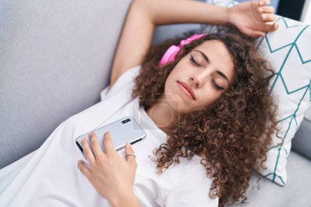 Photo for Young beautiful hispanic woman listening to music sleeping on sofa at home - Royalty Free Image
