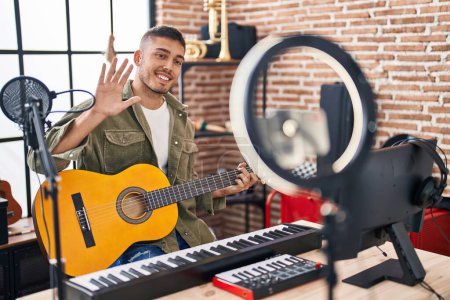 Photo for Young hispanic man doing online guitar tutorial looking positive and happy standing and smiling with a confident smile showing teeth - Royalty Free Image