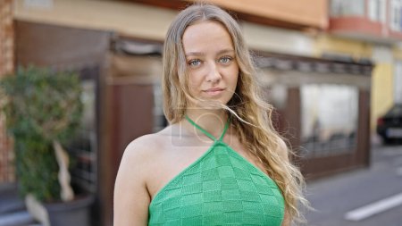 Téléchargez les photos : Jeune femme blonde debout avec une expression sérieuse à la terrasse du café - en image libre de droit