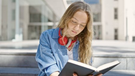 Téléchargez les photos : Jeune femme blonde étudiant livre de lecture assis sur les escaliers à l'université - en image libre de droit