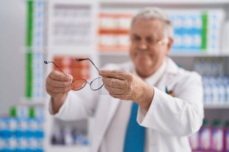 Photo for Middle age grey-haired man pharmacist smiling confident holding glasses at pharmacy - Royalty Free Image