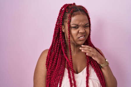 Foto de Mujer afroamericana con cabello trenzado de pie sobre fondo rosa expresión disgustada, disgustada y temerosa haciendo cara de asco porque la reacción de aversión. - Imagen libre de derechos