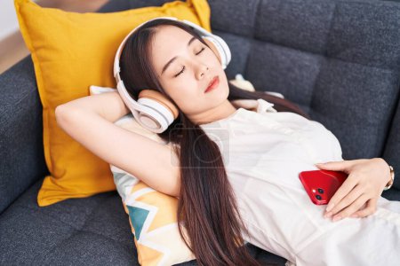 Téléchargez les photos : Young chinese woman listening to music sleeping on sofa at home - en image libre de droit