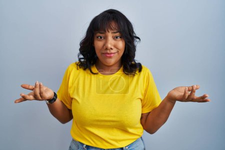 Photo for Hispanic woman standing over blue background clueless and confused with open arms, no idea concept. - Royalty Free Image