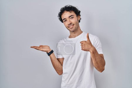 Téléchargez les photos : Homme hispanique debout sur fond isolé montrant la main de la paume et faisant un geste correct avec les pouces levés, souriant heureux et joyeux - en image libre de droit