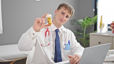Téléchargez les photos : Jeune homme caucasien médecin en utilisant des pilules de prescription d'ordinateur portable à la clinique - en image libre de droit